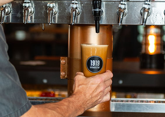 Beer tap just finished filling a "1919 Kitchen & Tap" labeled beer glass