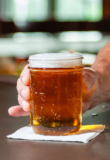 hand holding a glass filled with beer, resting on a table
