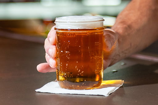 hand holding a glass filled with beer, resting on a table